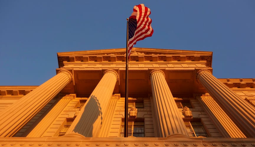 The front of the Commerce Department building, with four white columns and a U.S. flag