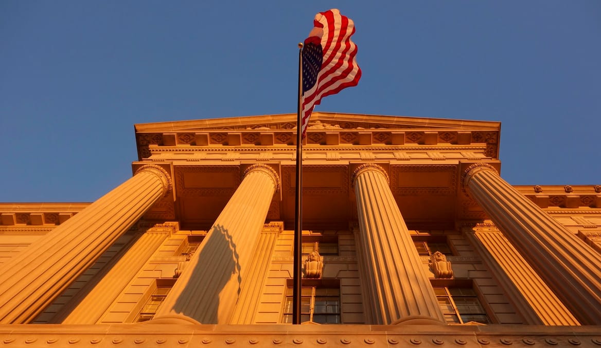 The front of the Commerce Department building, with four white columns and a U.S. flag