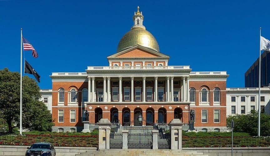 A stately capitol building with red brick, white columns and a golden dome under a bright blue sky