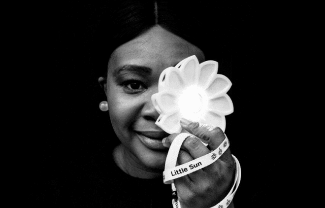 A black and white photograph of a women with dark hair and medium skin holding a light flower in front of her face