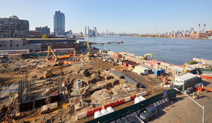 Construction crews excavate a large property on Brooklyn's riverfront, with the Manhattan skyline in the distance