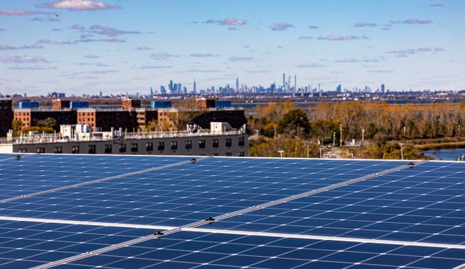 Rooftop solar panels cover an affordable apartment building in Queens; the Manhattan skyline is seen on the horizon
