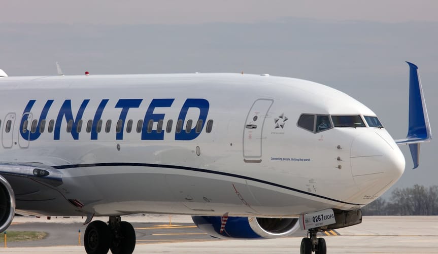 A white airplane with the blue United logo taxis on an airport runway