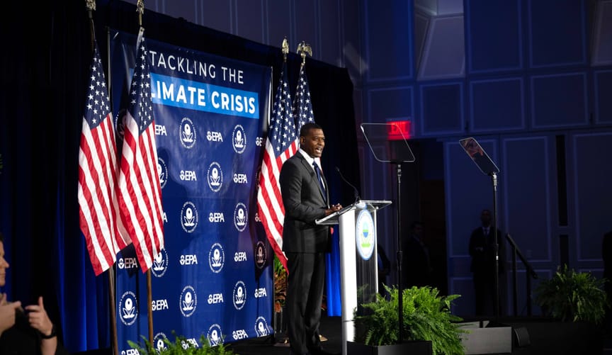 EPA Administrator Michael Regan at a lectern on a stage with flags