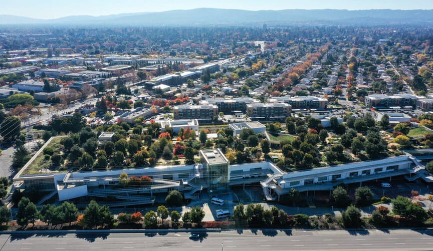 an aerial view of a town with many corporate buildings, forested hills in the distance