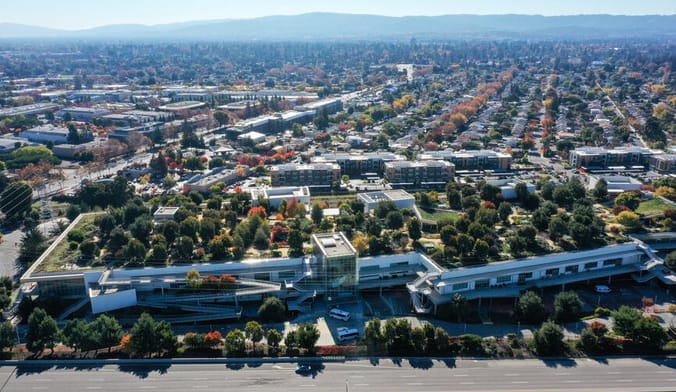 an aerial view of a town with many corporate buildings, forested hills in the distance