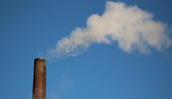 A white cloud of smoke rises from a tall smokestack