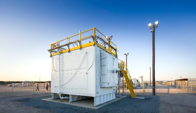 A large white metal box with yellow stairs positioned at an outdoor industrial site