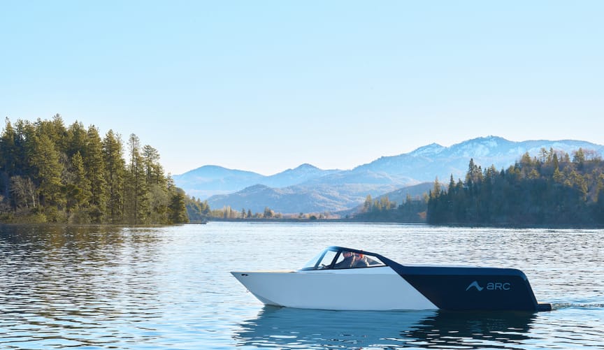 A man and a women sit in a black and white speedboat on a mountain lake