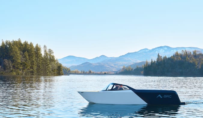 A man and a women sit in a black and white speedboat on a mountain lake