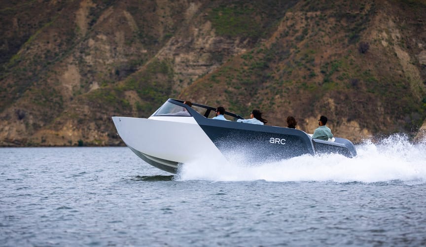 A small group of people rides in a speedboat on a body of water next to mountains