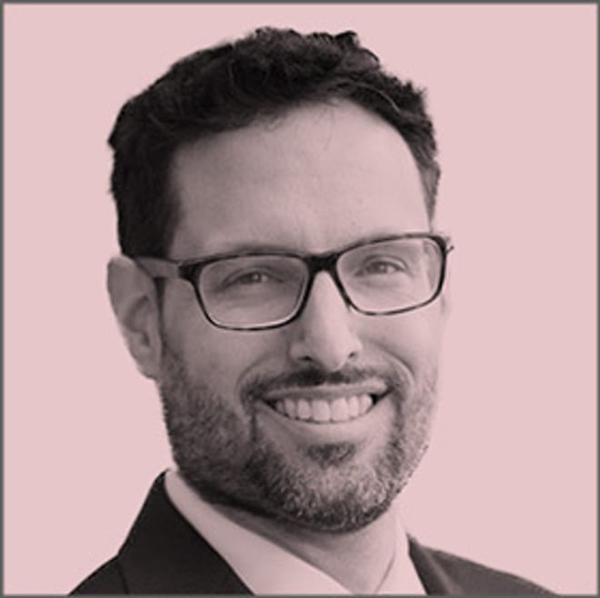 A smiling man with glasses and a short beard in a pink-tinted photo