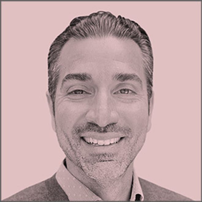 A smiling man with short hair and a light beard in a pink-tinted photo