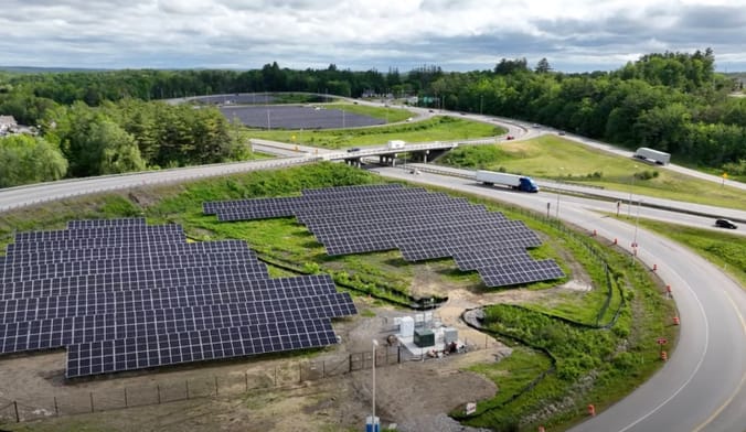 An solar array is situated next to a highway interchange in a moderately wooded area