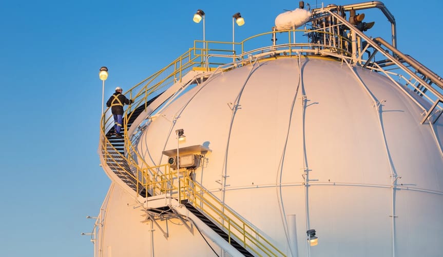 Person with hard hat and safety attire walks up stairs that scale a spherical tank at a hydrogen facility.