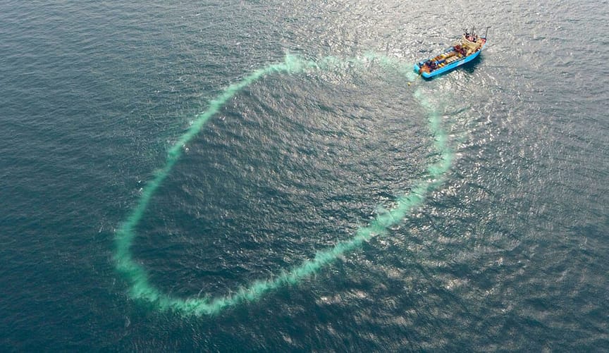 A circle of underwater bubbles next to a blue boat in the ocean
