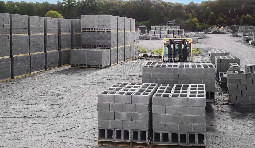 Stacks of gray concrete blocks sit on pallets in a dusty industrial lot.