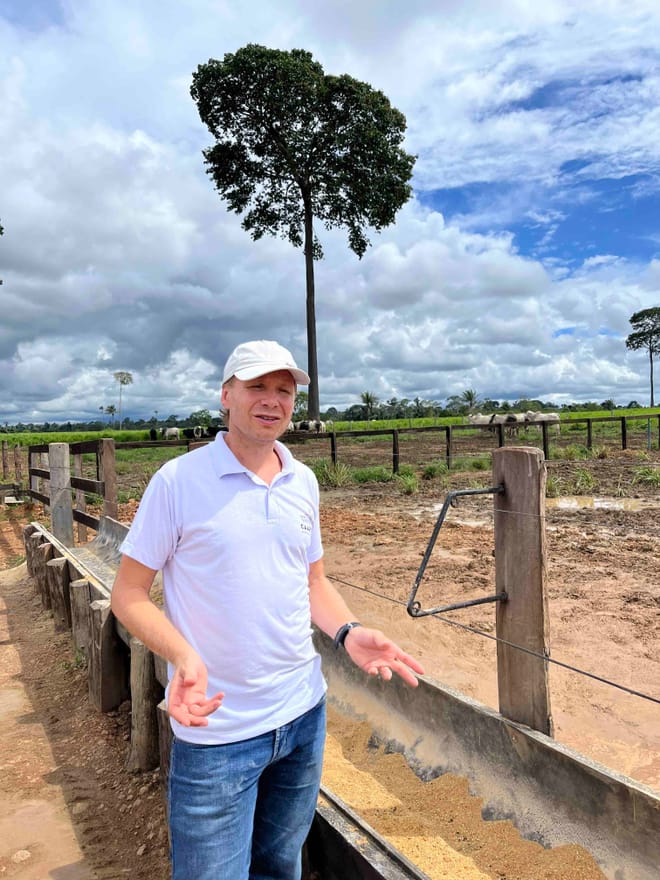 A man in a white polo shirt, white cap and jeans stands near a fence with his hands upturned