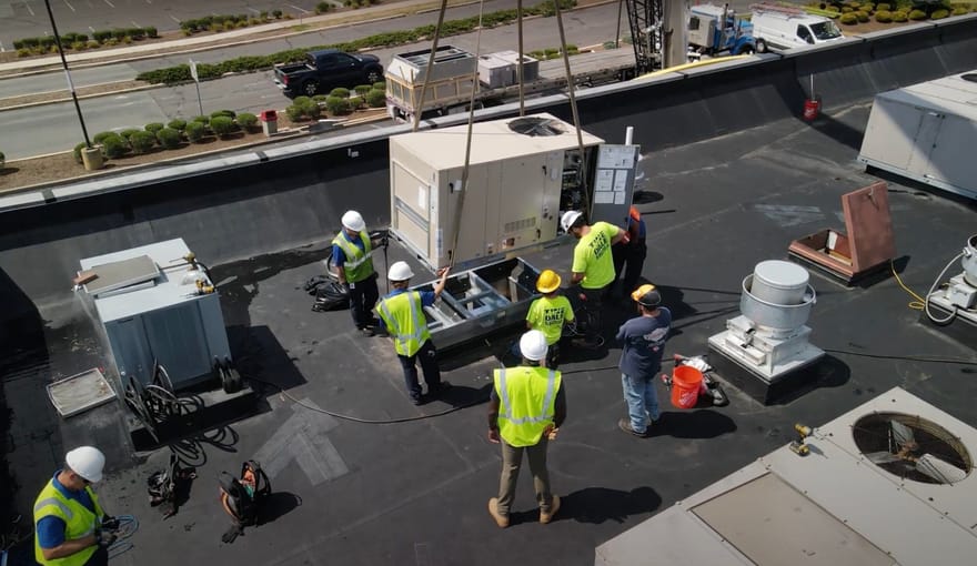 Workers installing a rooftop HVAC system at a small commercial building.