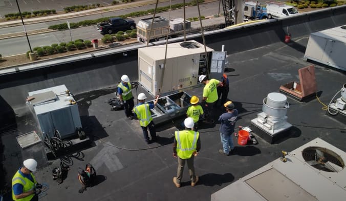 Workers installing a rooftop HVAC system at a small commercial building.