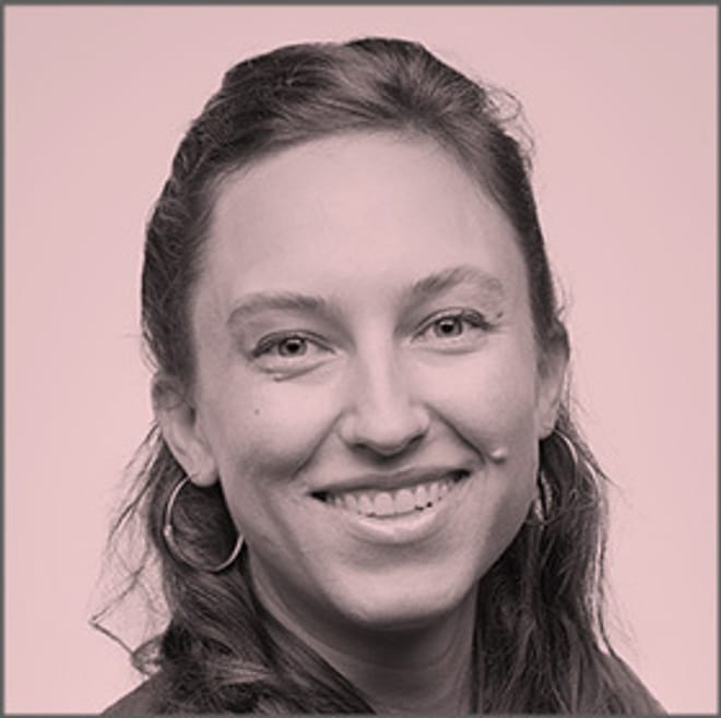 A smiling with long hair partially pulled back and large hoop earrings in a pink-tinted photo