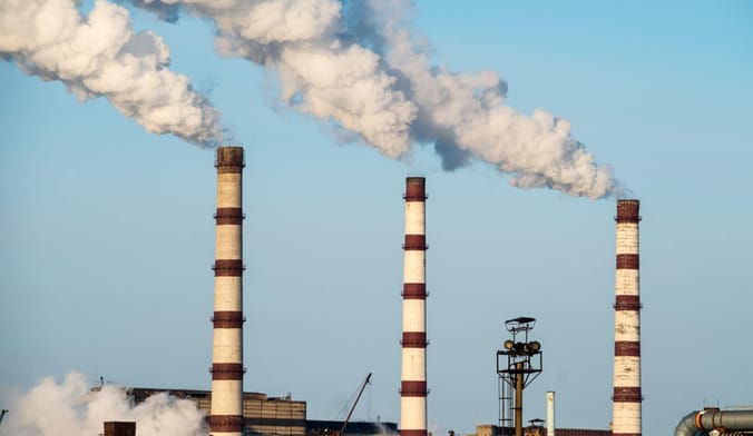 Smoke plumes arise from three tall striped coal stacks at a power plant
