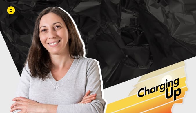 A smiling woman with shoulder length brown hair and a light skin tone in a V-neck sweater. Graphic overlay says CHARGING UP.