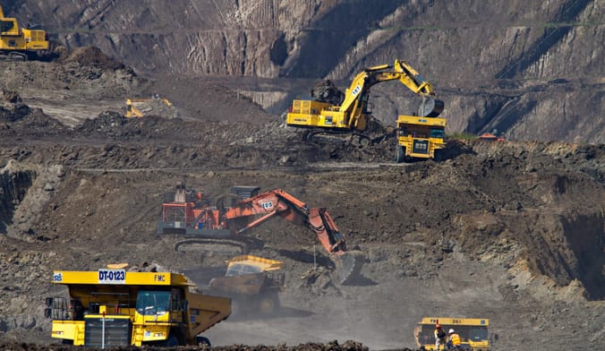 Several yellow bulldozers scoop earth in a coal mine
