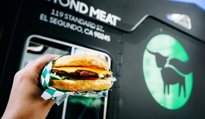 A hand holds up a burger next to a sign that says beyond meat
