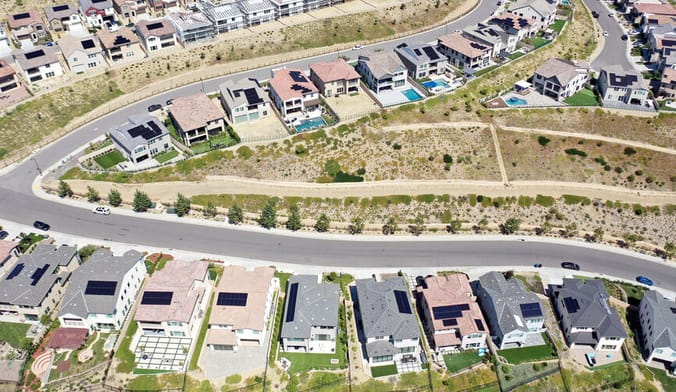 An aerial view of a subdivision of single-family homes, many with solar panels visible on the roof