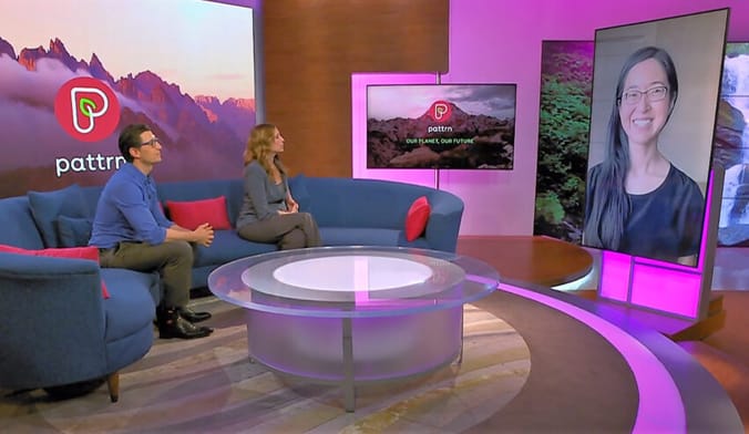 Two people sitting on a couch engage in conversation with a woman with long black hair and eyeglasses who is on video