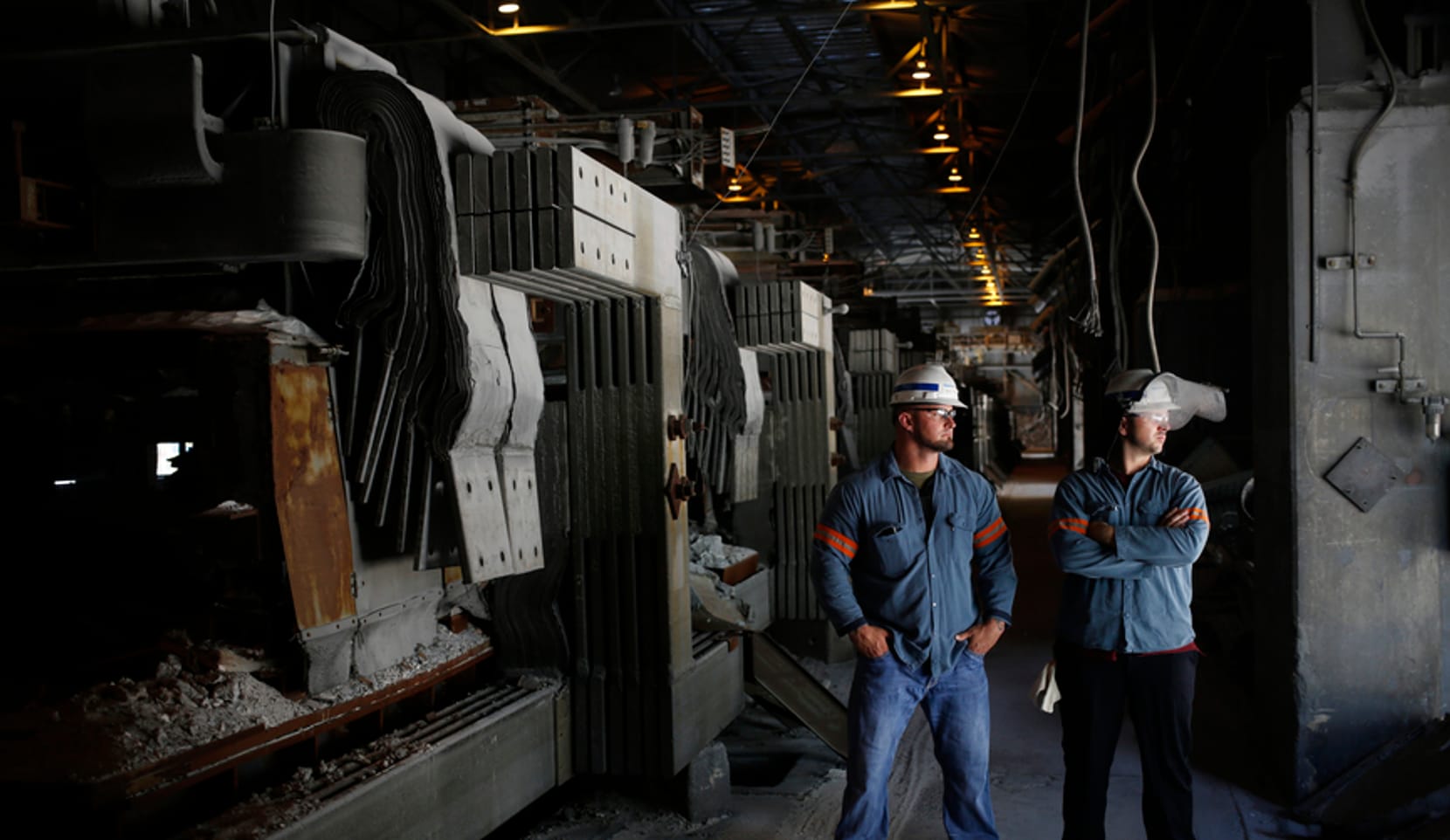Two men in work gear and hard hats stand inside a factory