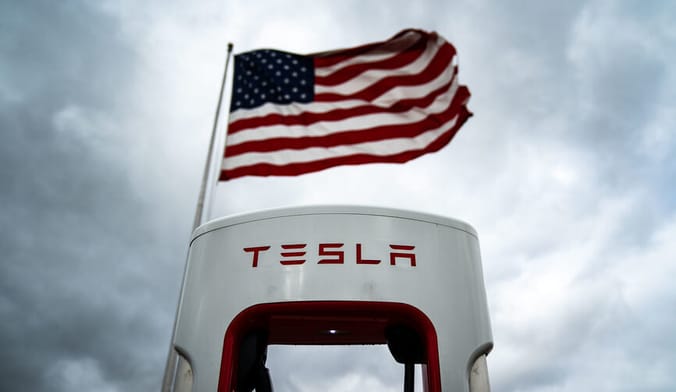 AN American flag is shown flying behind a tesla EV charger