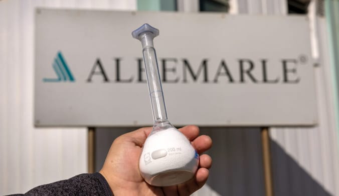 a hand holding a glass flask containing a white powdery substance