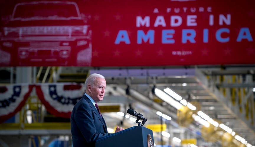 A man with white hair wearing a blue suit speaks at a lectern under a sign that reads "A future made in America"