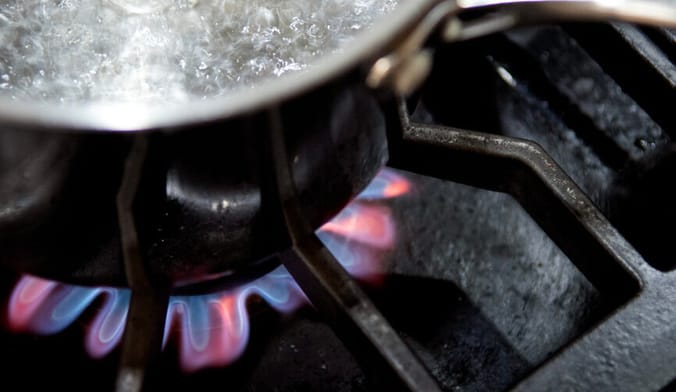 Closeup photo of a pot of water boiling on a gas stove with pink and blue flames visible
