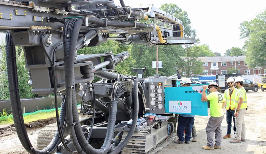Several workers in safety gear stand next to a very large piece of industrial equipment