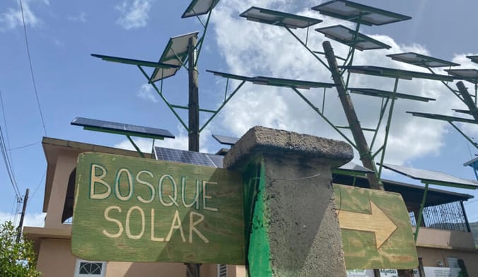 Solar panels on poles jutting up at many different angles behind a sign that says Bosque Solar and an arrow pointing right