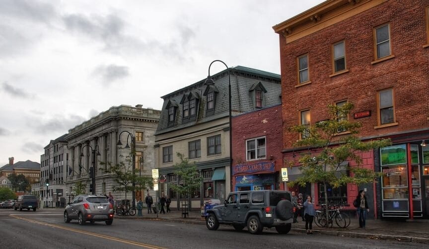 a street with old multistory brick buildings, cars and pedestrians