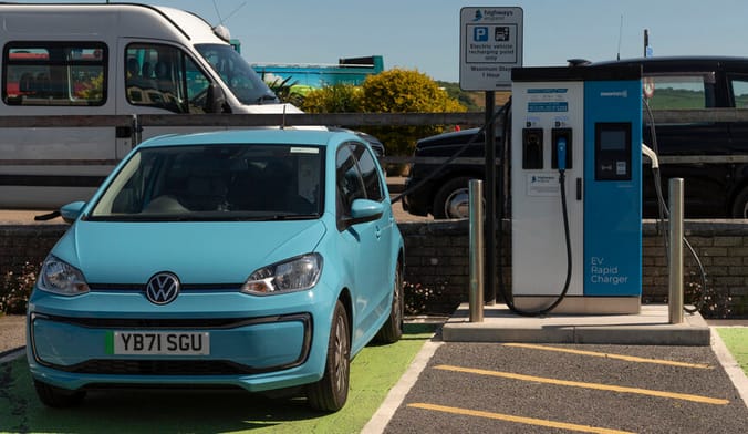 A small blue Volkswagen EV plugged into a public charging station