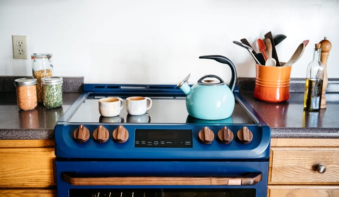 A blue induction range with two mugs and an aqua kettle sitting on top