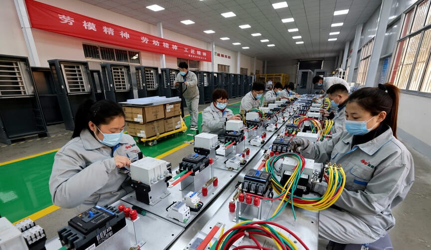 Chinese workers wearing blue face masks stand at an assembly line working on electronic components