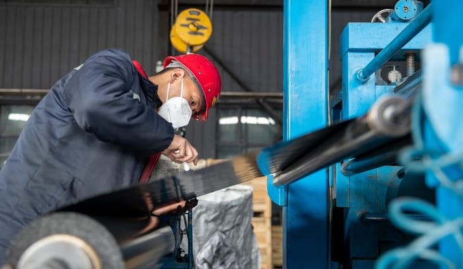 a Chinese worker wearing safety gear and a hard hat works on the assembly line of a graphite factory