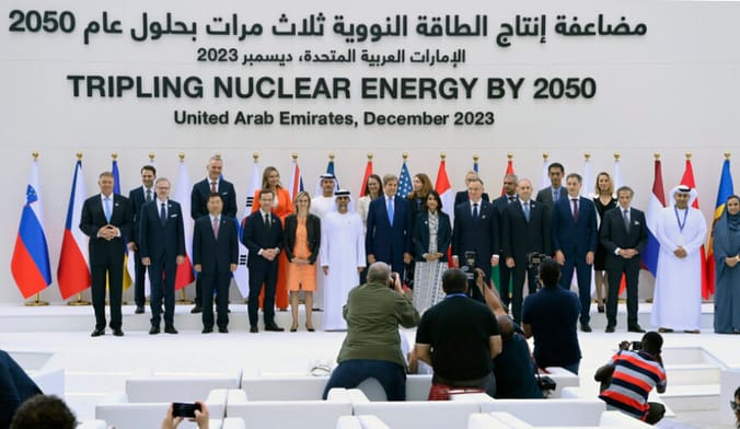 Dignitaries and diplomats stand on a stage lined with national flags under the words TRIPLING NUCLEAR ENERGY BY 2050