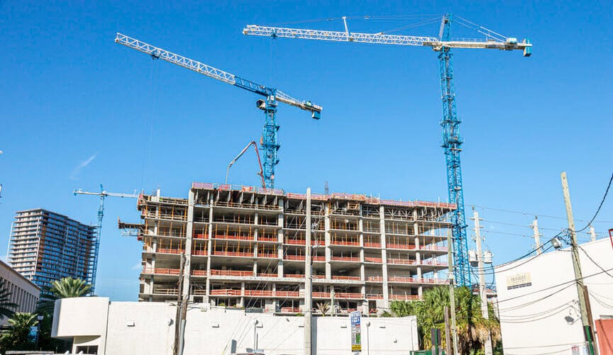 Two large cranes sit next to a building under construction against the backdrop of a bright blue sky