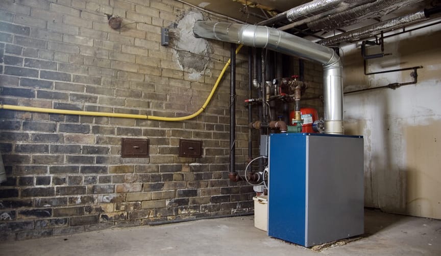A large blue furnace sits in the corner of a brick-walled, somewhat dilapidated basement