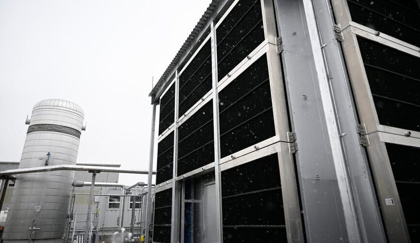 A large industrial facility with a large cylindrical tank in the background under a gloomy gray sky