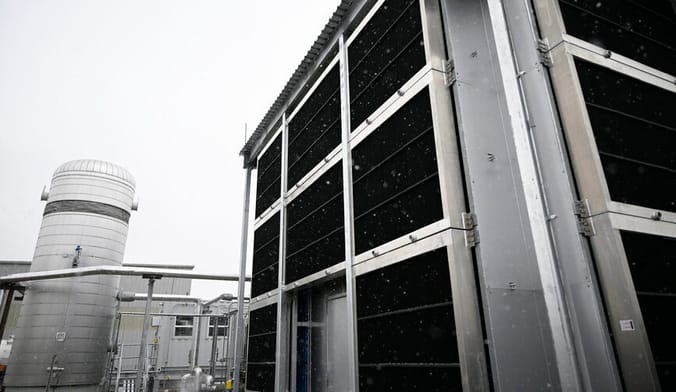 A large industrial facility with a large cylindrical tank in the background under a gloomy gray sky