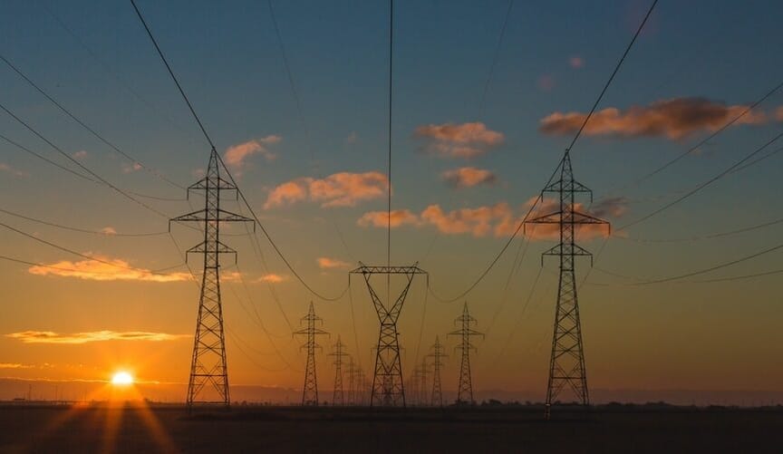 large transmission lines and pylons set against the backdrop of a dramatic blue and orange sunset