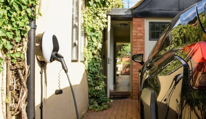 An EV is plugged into a wall-mounted charging unit in front of a home